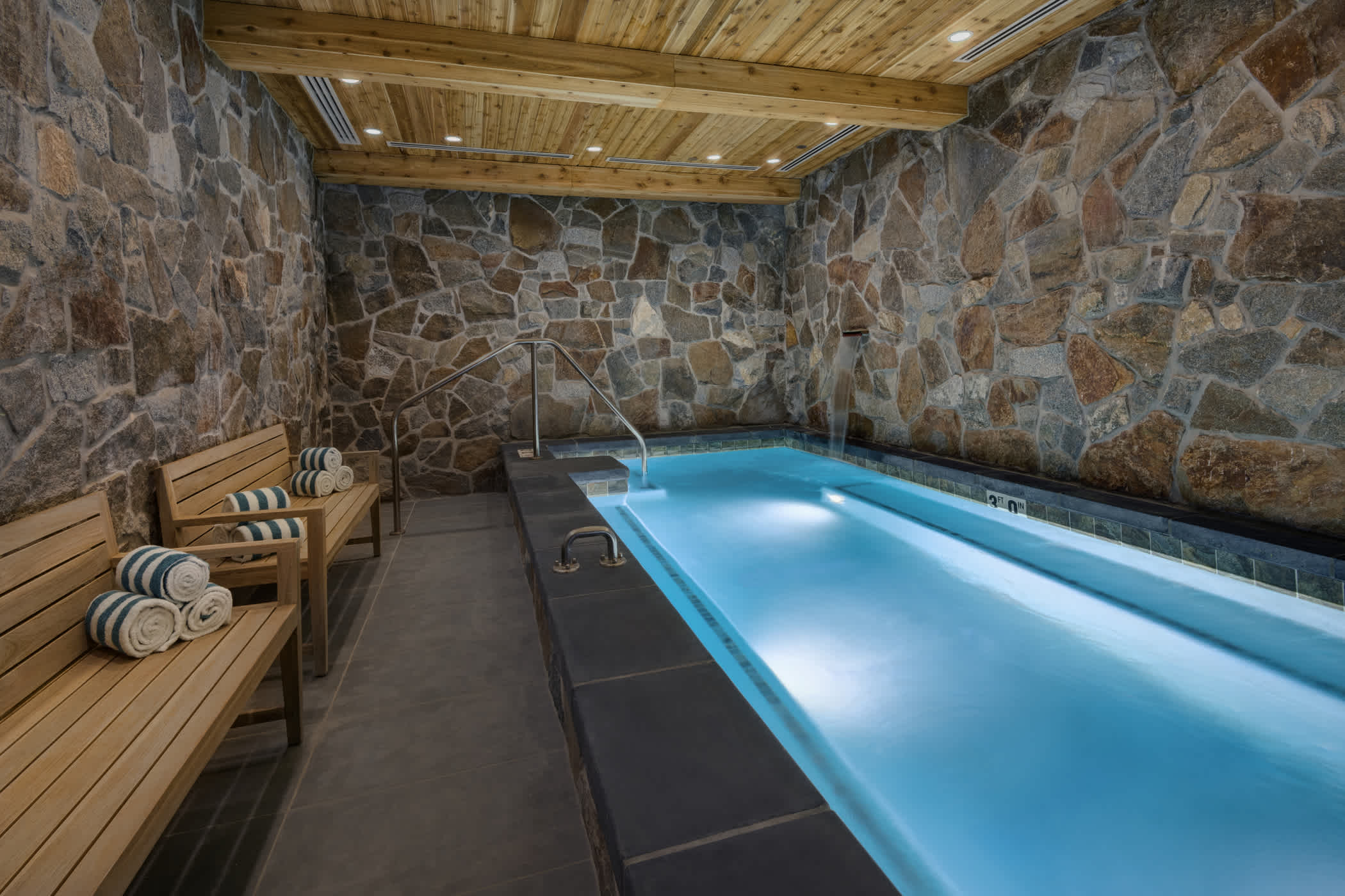 An indoor rock grotto with hot tub is surrounded by benches and fresh towels in the Snowpine spa