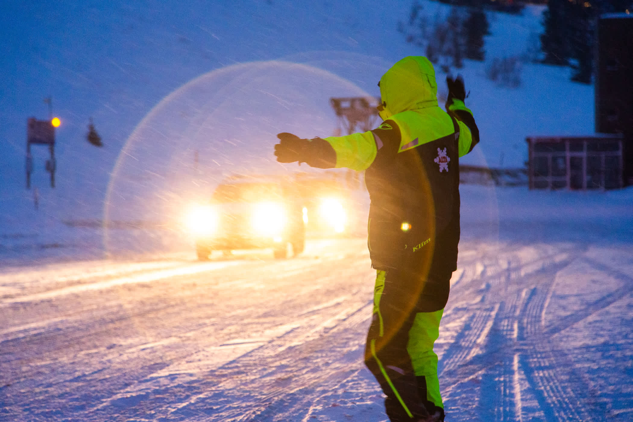 A parking attendant in a bright vest guides a vehicle to a parking space in a snow storm