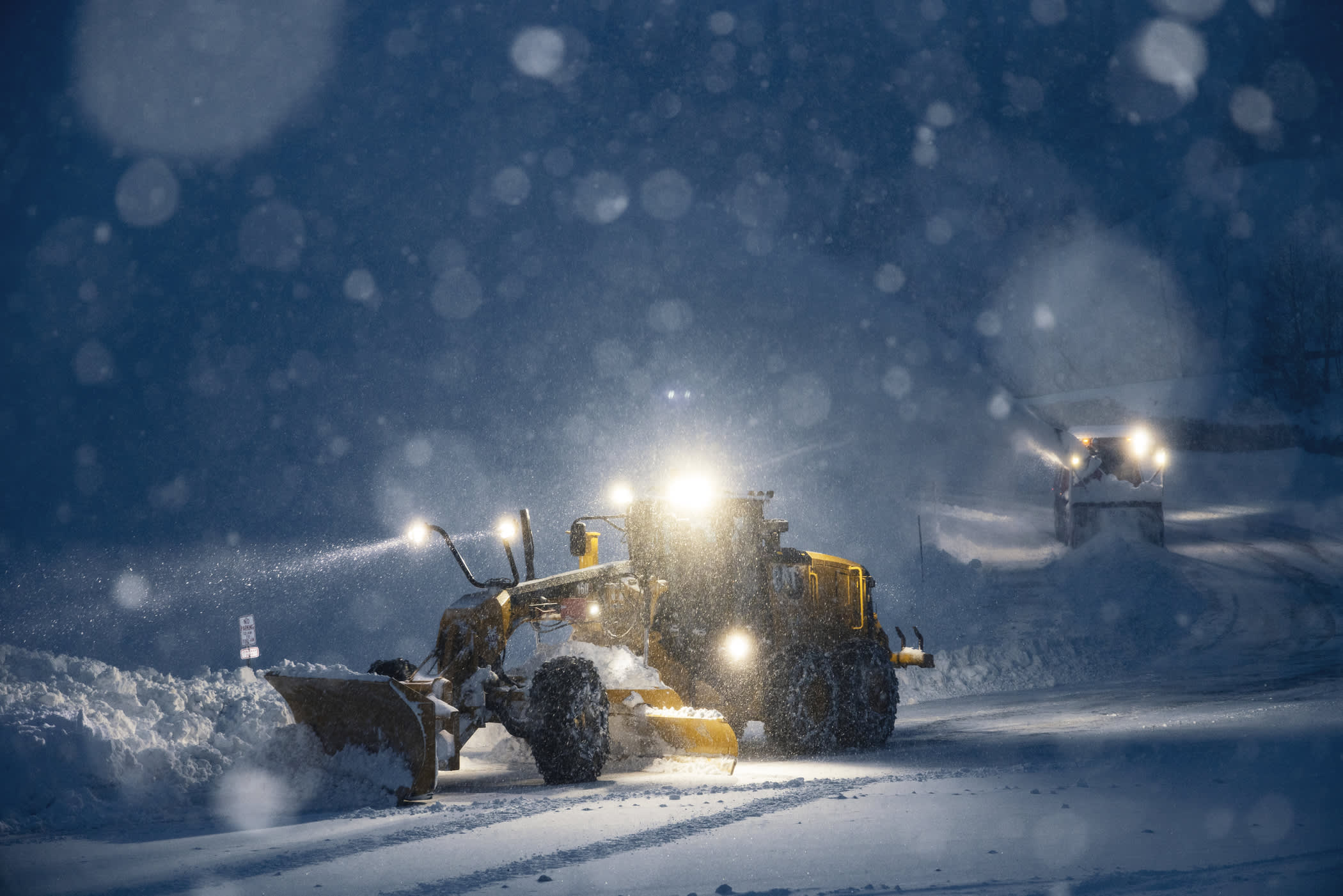 Two plows remove snow at night while a snowstorm rages