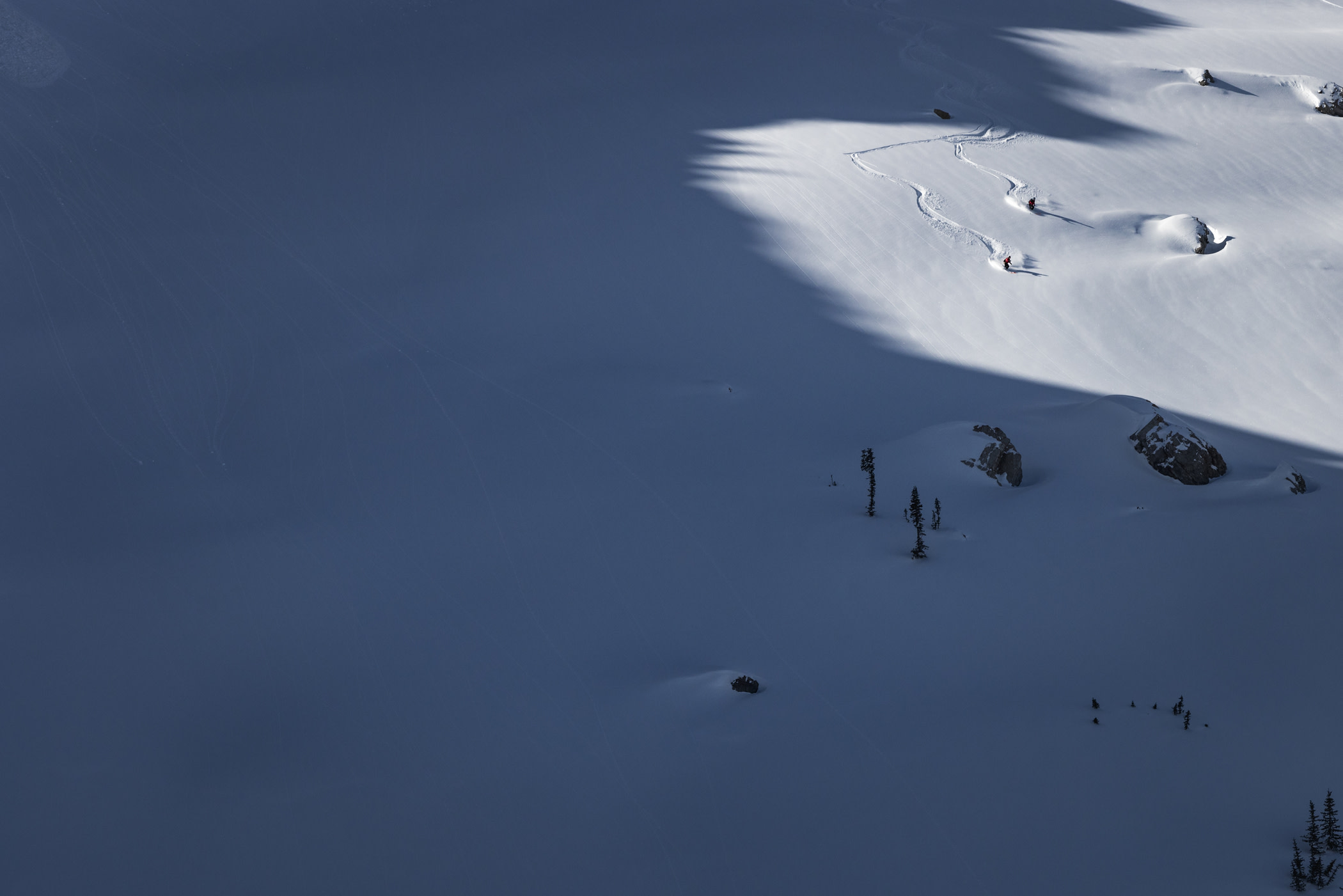 Two ski patrollers ski down a snowy mountain in dramatic natural light