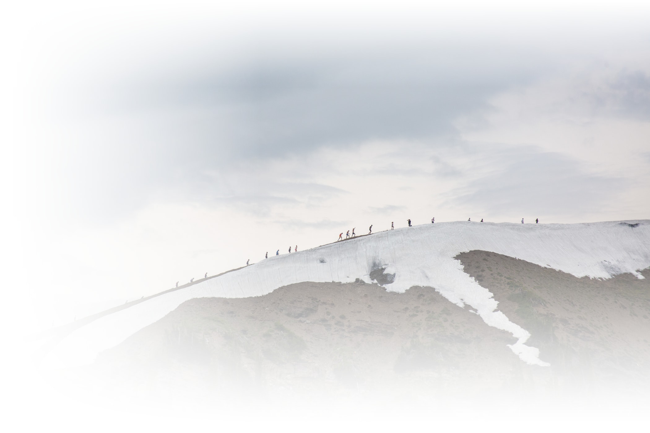 Runners cross a snow patch on a mountain ridge at Alta Ski Area on a sunny summer day