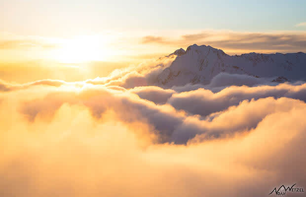 Mountain rising above thick clouds with amber sunset sky