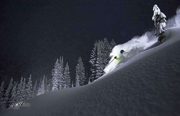 Skier illuminated skiing deep snow at night with clear starry sky