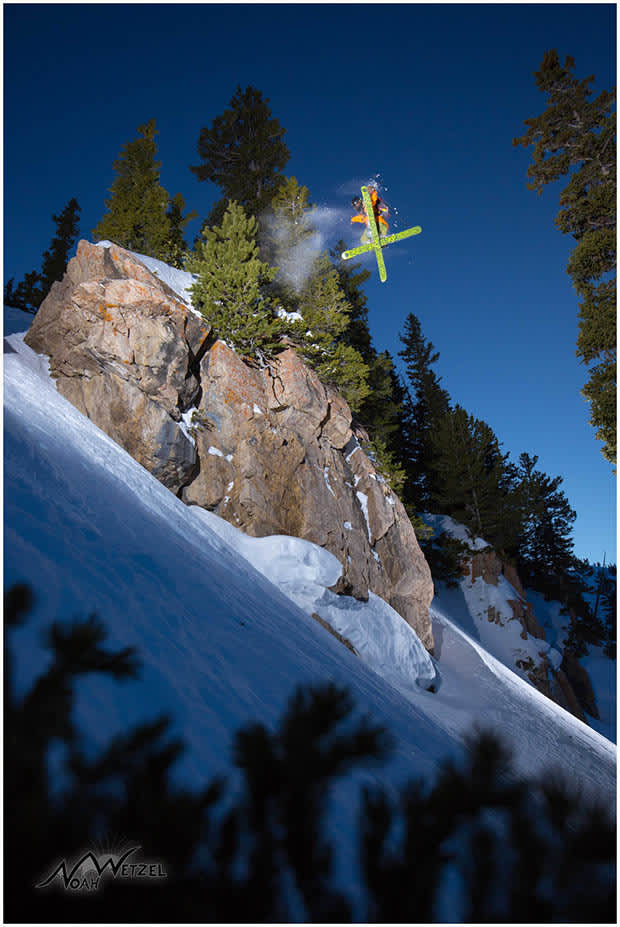 Skier jumping off clif face with fresh snow and clear blue sky