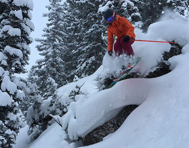 Skier girl jumping off short cliff with fresh snow