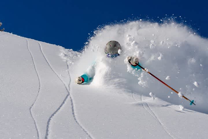 Skier in teal coat skiing deep fresh snow