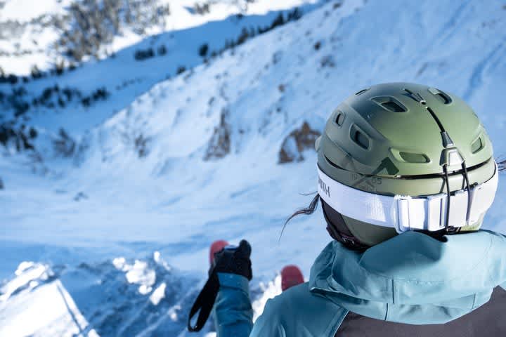 Woman with green helmet looking down steep ski run