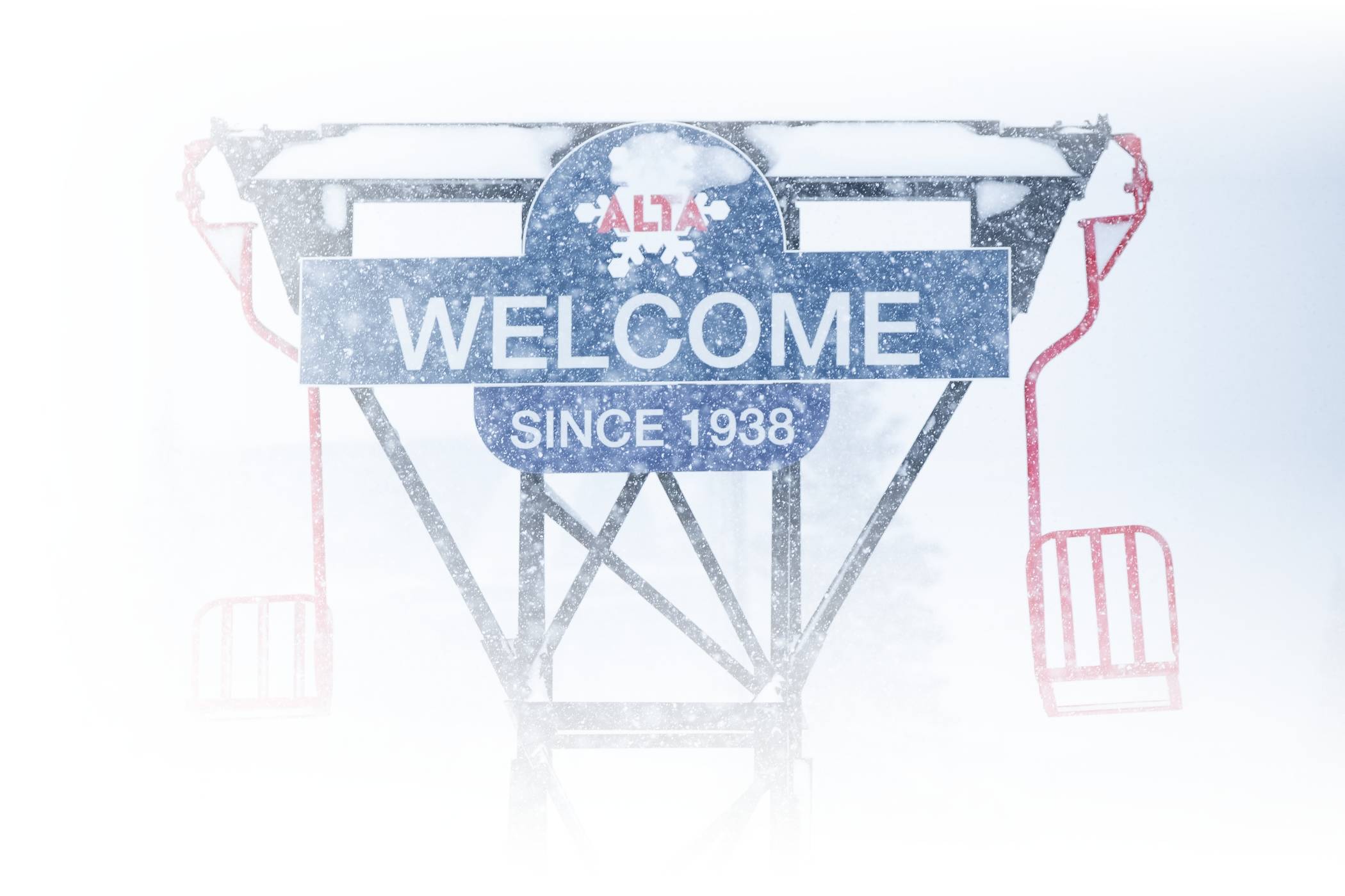 Snow falling on the Welcome to Alta sign and old Collins single chairs at the base of Alta