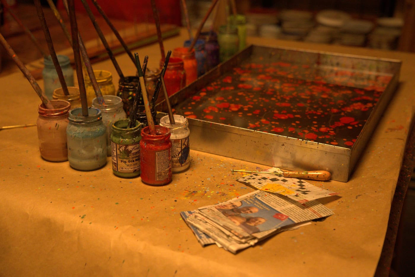 The marbling tray with red colour floating on the water, brushes in jars beside it