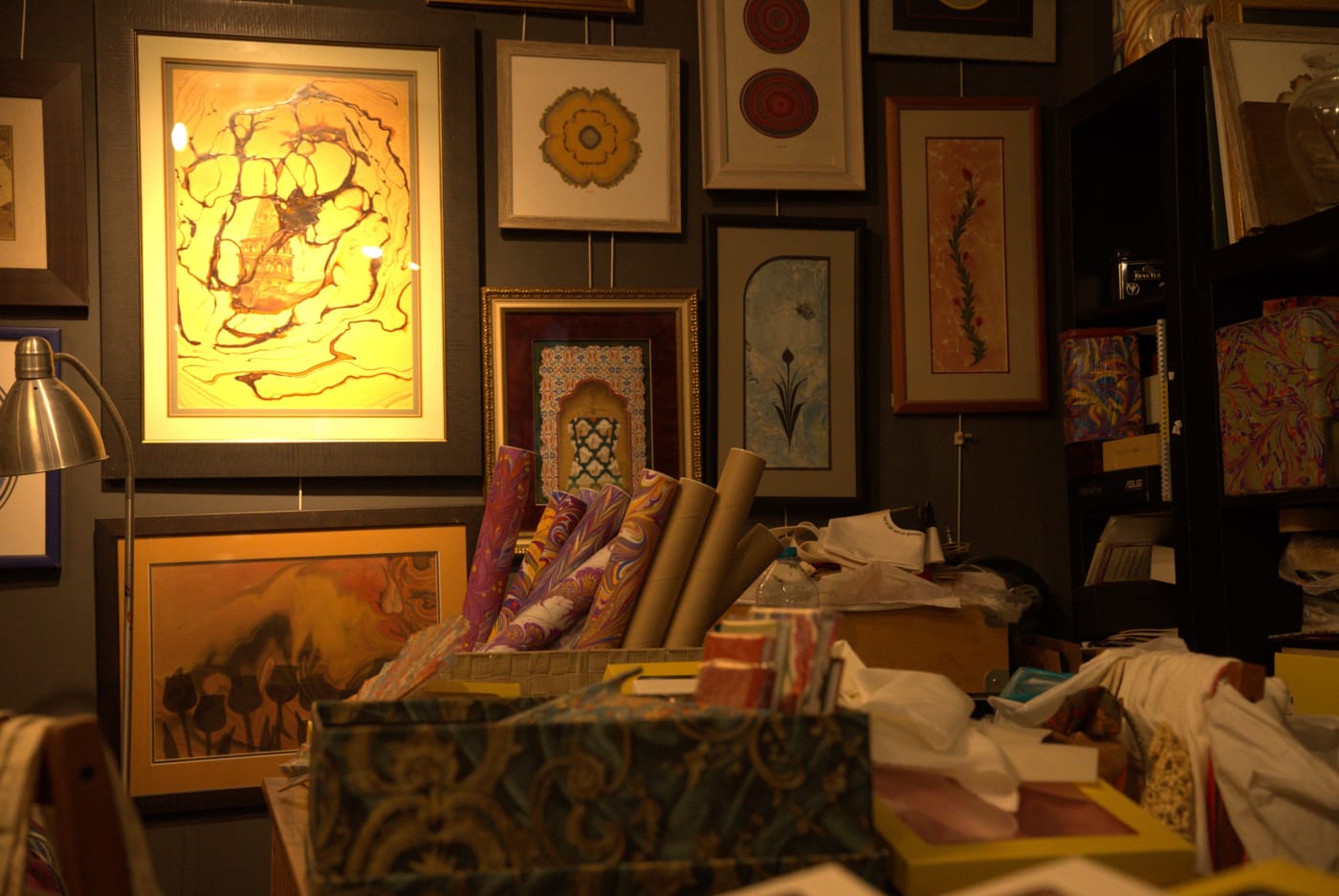 Framed ebru works on the atelier wall under a lamp