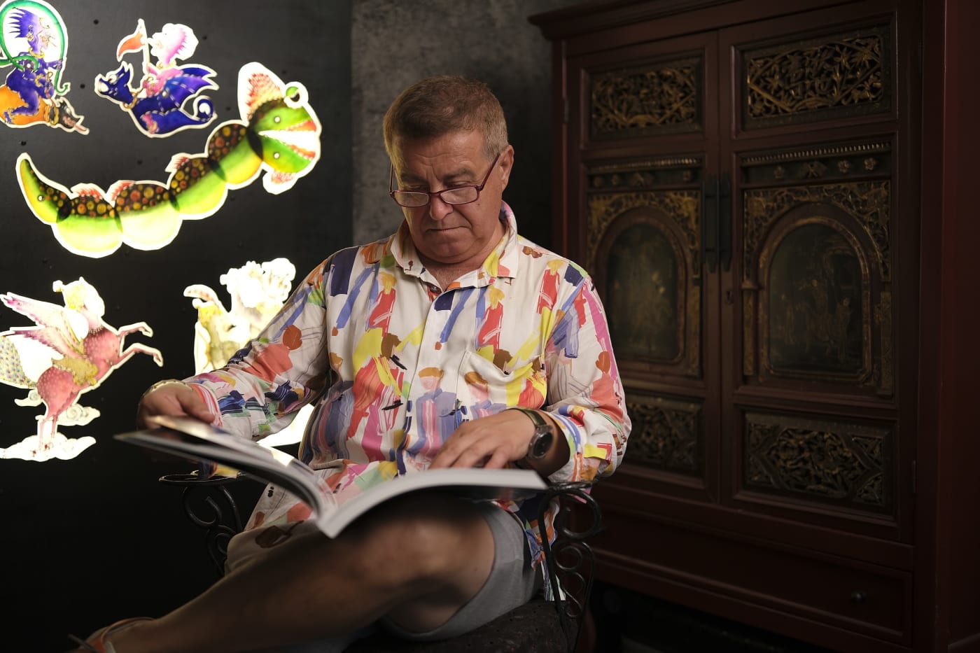 Cengiz Özek in his atelier with translucent Karagöz figures lit on the wall behind him