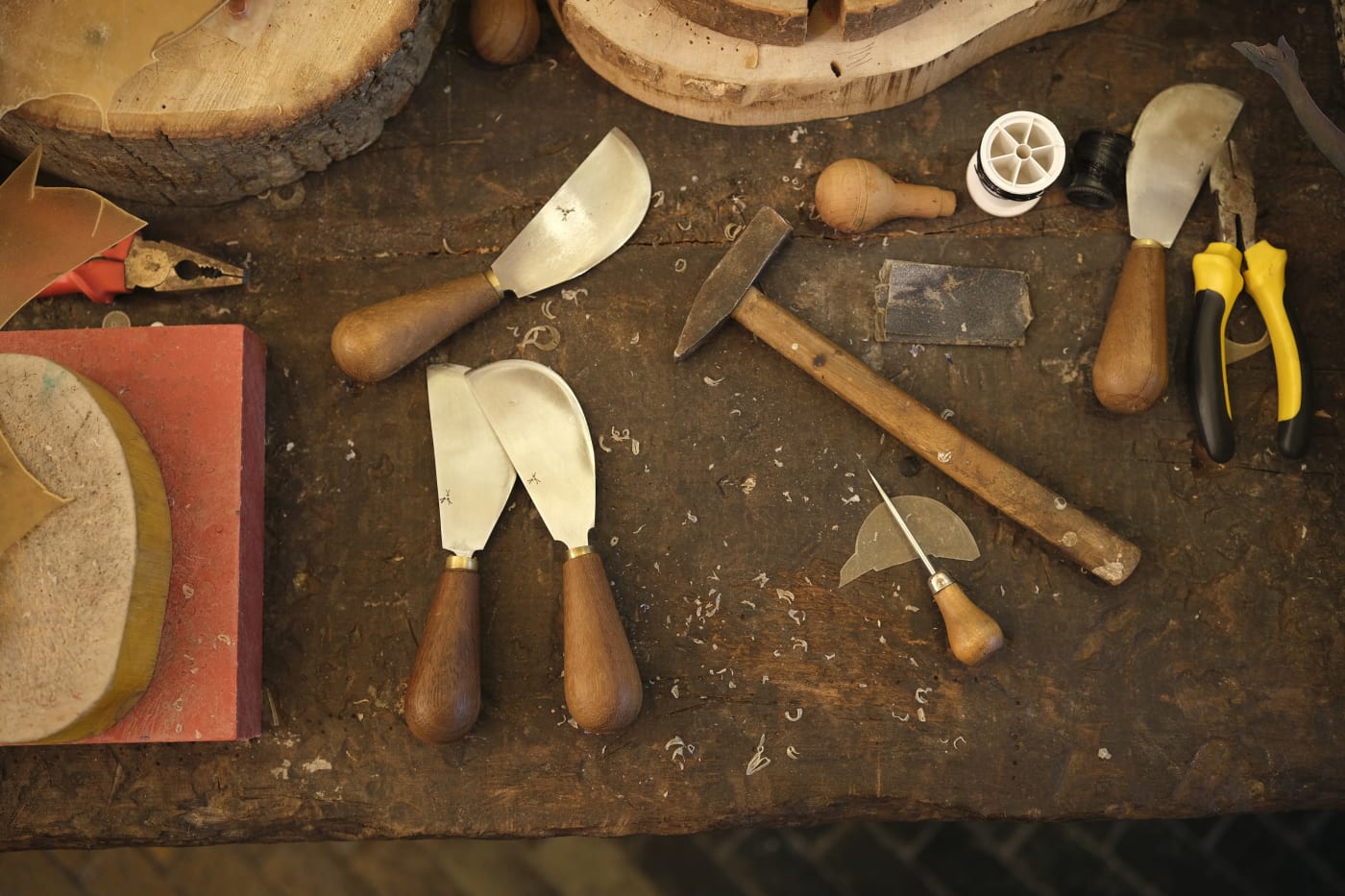 Curved leather knives, a small hammer and an awl on the atelier workbench