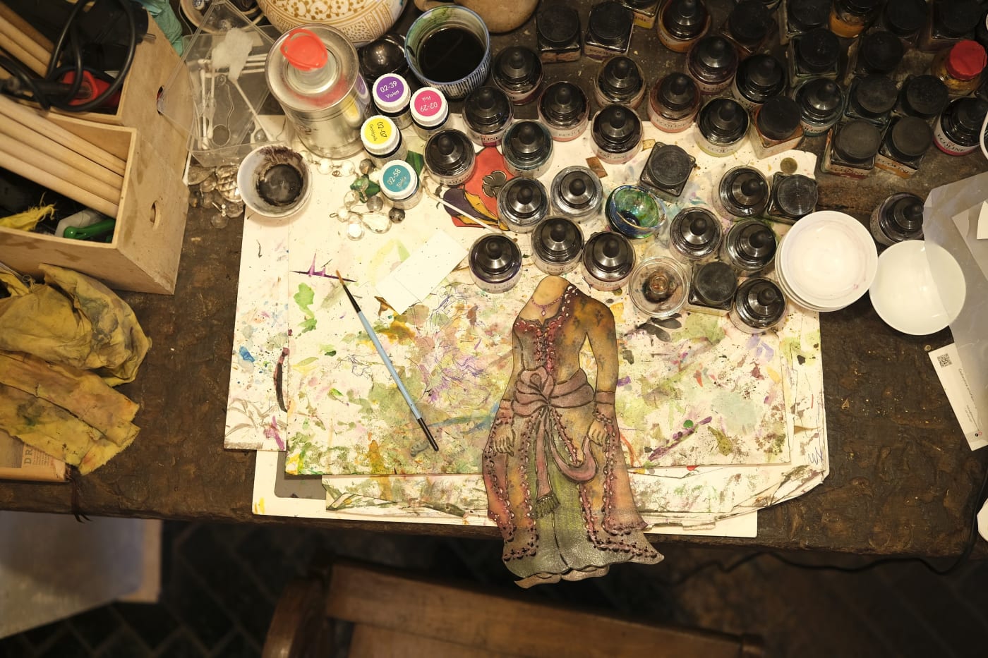 A half-painted Karagöz figure among pots of translucent paint