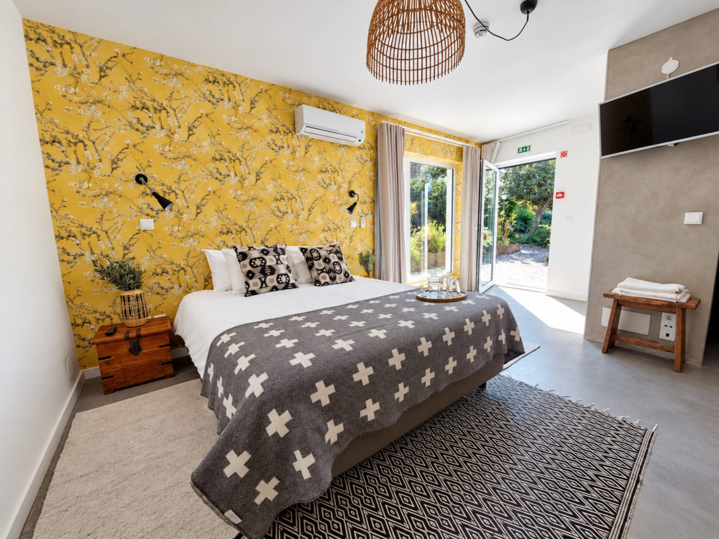 Quarto da Vila Louro com parede floral amarela e cama cinzenta, em Santa Cruz