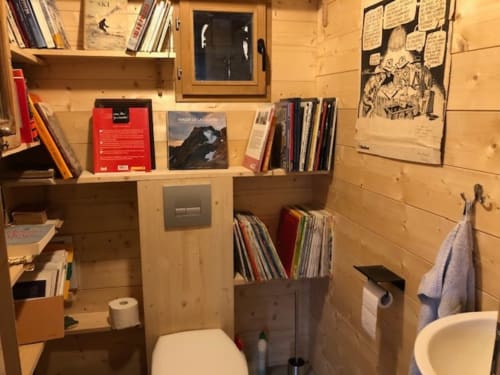 Compact bathroom in Les Chalets de l'Eau Rousse cottage with toilet, shelving, books, and mountain lodge décor