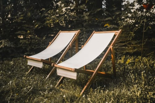 Deux chaises longues en bois avec tissu blanc dans un jardin luxuriant du gîte ART DE VOYAGER à Étretat