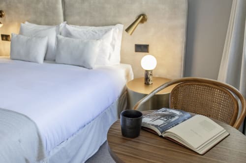 Quarto de hotel moderno na Benefit Collection Porto com roupa de cama branca, escrivaninha de madeira, cadeira de rattan e luminária de criado