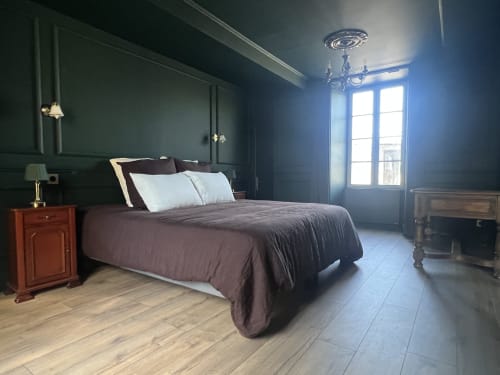 Chambre élégante à La Millière aux murs bleu-canard, lit queen-size avec draps bordeaux, table de nuit en bois, et lumière vive