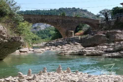 Puente medieval de piedra atravesando río turquesa con rocas apiladas, montañas verdes del Prepirineo de fondo, apartamento