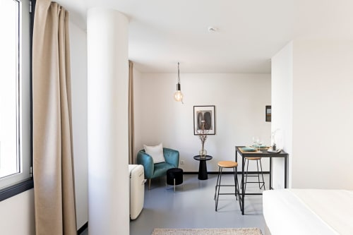 Moderno estúdio na Benefit Collection Porto com poltrona azul-petróleo, mesa preta, kitchenette e vista para a cidade