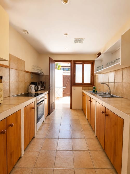 Amplia cocina de galería en Villa Paloma, Corralejo, con gabinetes de madera, piso de azulejo beige y acceso a patio