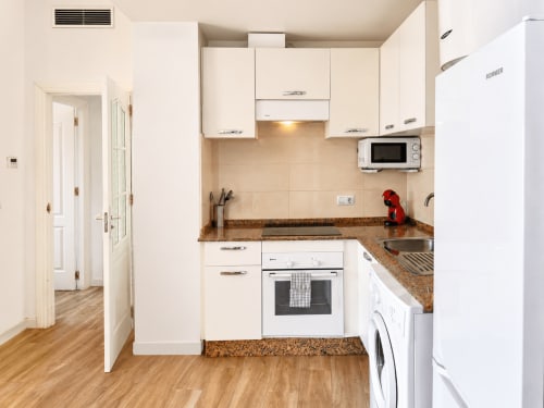 Modern white kitchen with brown granite countertops, oven, microwave, and washing machine in Apartamento Frontal Coral at
