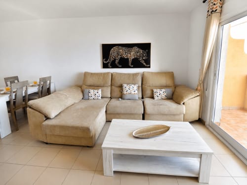 Amplia sala de estar en Apartamento Frontal Sol con sofá seccional beige, mesa de café blanca y obra de arte leopardo