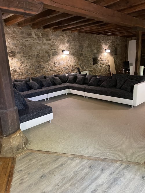 Élégant espace lounge avec canapé sectionnel en tissu foncé, murs en pierre apparente, poutres en bois et éclairage encastré aux Chambres