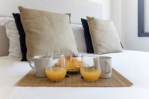 Cama no estúdio Benefit Collection Porto com bandeja de café da manhã: suco de laranja, croissants, xícaras de café sobre tapete de madeira