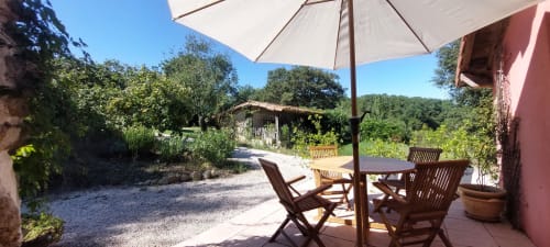 Garden patio at Les Gites de Campardon cottage with wooden furniture, umbrella shade, and countryside views in Monties,