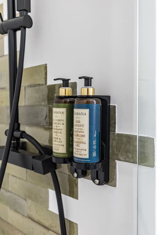 Dispenser preto fixado na parede com dois frascos de produtos de higiene Damana no banheiro de hotel no Porto