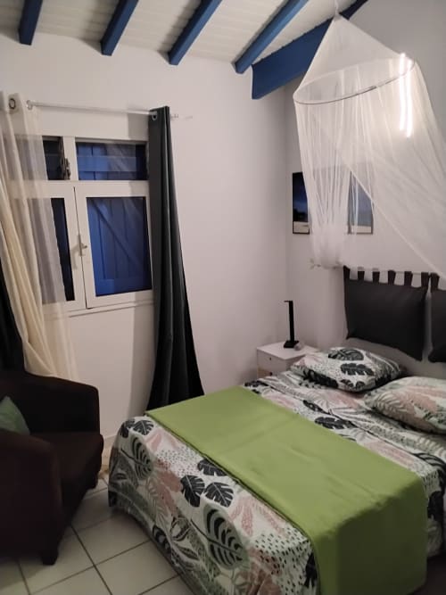 Chambre twin du Kay Betty avec lits jumeaux, parure verte, moustiquaire, climatisation et vue mer à Les Trois-Ilets