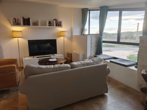 Salon moderne avec canapé beige, télévision écran plat et vue panoramique sur la rivière à la Magnanerie de Sainte Croix