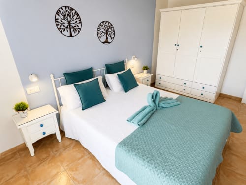 Modern bedroom at Apartamentos El Calón Playa with teal pillows, white bedding, wooden furniture, and decorative wall art