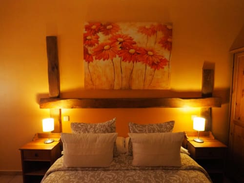 Cálida habitación con cuadros de margaritas rojas sobre cabecera de madera, lámparas de mesita de noche brillantes y paredes con acentos naranjas