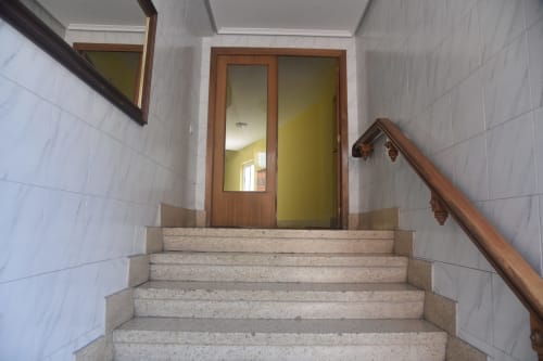Staircase in central Benavente apartment with white tile walls and wooden door leading to yellow room