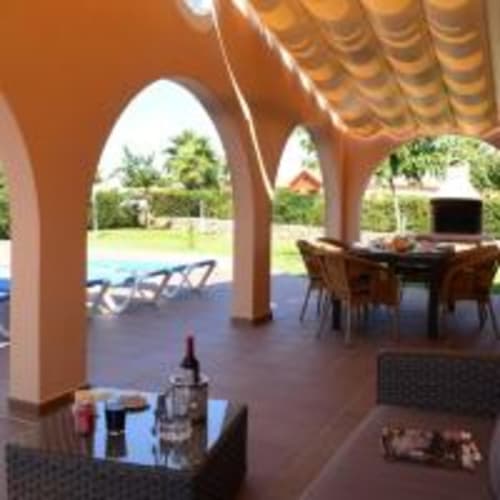 Terraza cubierta con columnas arqueadas en villa Las Golondrinas, con vistas a piscina y jardines tropicales en Cap d'Artrutx