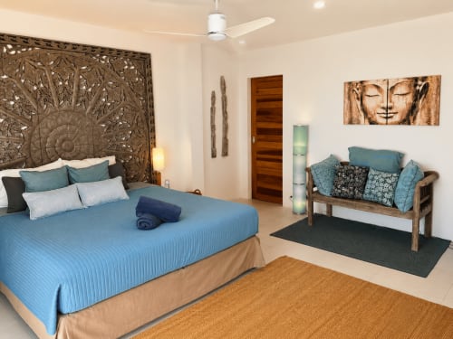 Spacious master bedroom at Indigo Villa Samui with blue bedding, carved wooden headboard, and sitting area on Ko Samui