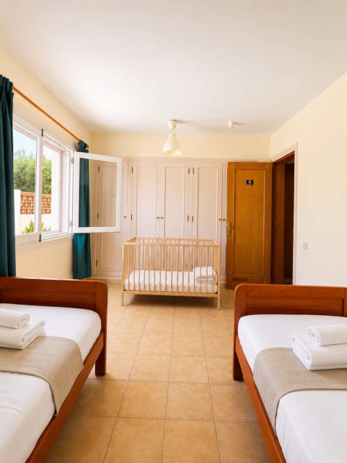 Amplio dormitorio de villa en Sara & Gino Fuerteventura con dos camas de madera, cuna, armarios empotrados y acceso a terraza