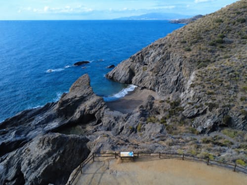 Rocky coastal cliffs with beach cove and viewpoint railing at Apartamentos El Calón Playa, Cuevas del Almanzora, Spain