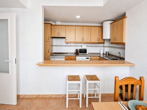 Modern kitchen with wooden cabinets, breakfast bar, and white bar stools in Apartamento Lateral at Apartamentos El Calón