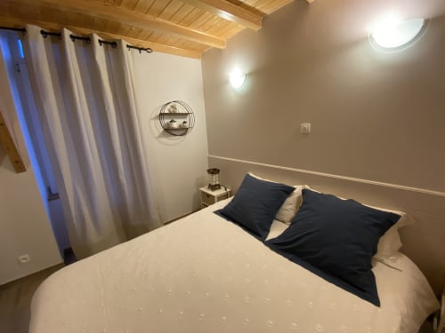 Chambre douillette au Cocon De Curson avec lit queen-size, oreillers noirs, plafond en bois, appliques murales et fenêtre voilée