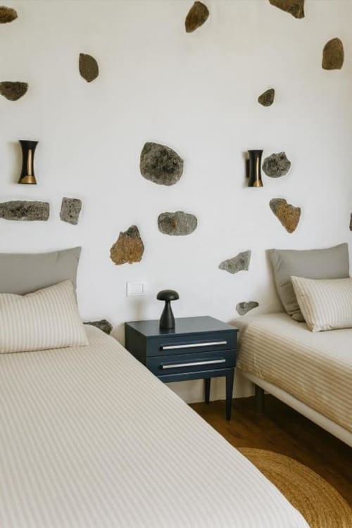 Camas gemelas con ropa de cama a rayas en villa Nexus de Rural La Palma, con arte de pared en piedra decorativa y mesita de noche oscura.