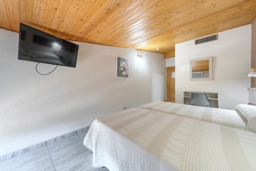Habitación doble de Hostal El Molino con dos camas, techo de madera, TV y escritorio en Collado Villalba