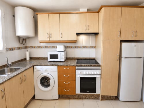 Cocina equipada con muebles de madera, encimeras de granito, lavadora, horno y refrigerador en Apartamentos El Calón