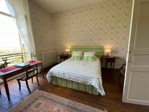 Chambre élégante au Château de Vaux Morvan avec literie rayée, papier peint floral, vue sur les jardins et mobilier d'époque