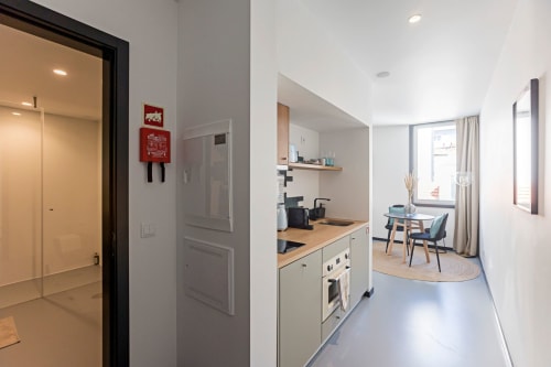 Studio moderno no Porto com cozinha equipada, bancada de madeira, eletrodomésticos brancos e sala de estar aberta com cadeiras de jantar e vista para a cidade