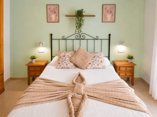 Dormitorio espacioso en Apartamentos El Calón Playa con cama de hierro forjado, mesitas de madera y paredes verde salvia