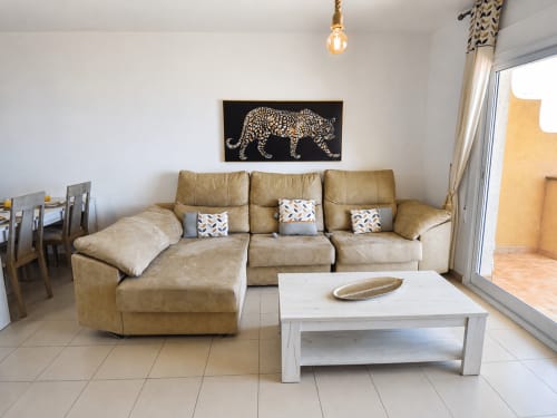Amplio salón en Apartamentos El Calón Playa con sofá seccionado beige, mesa de centro blanca y obra de arte con leopardo