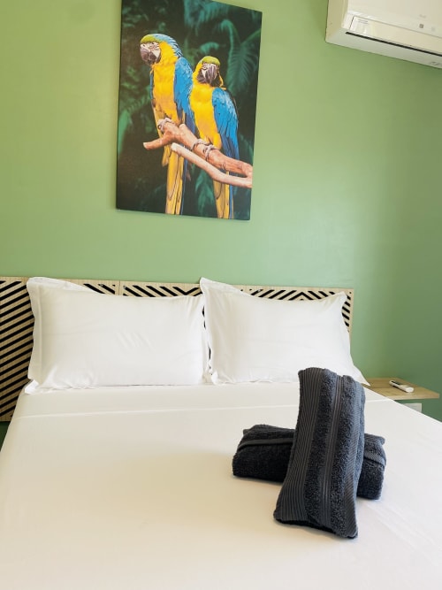 Chambre moderne avec literie blanche, serviettes noires et tableau de perroquet vibrant au-dessus d'une tête de lit zébrée chez Maisons En Or